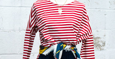 Red and white striped tee shirt, nautical belt, and navy windowpane shorts on a manequin against a white brick background