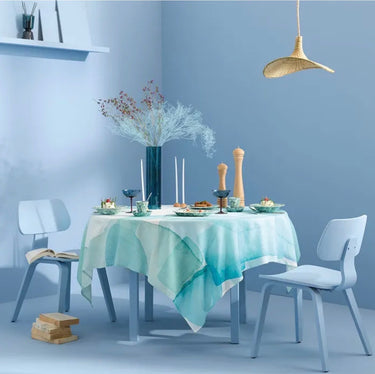 Dining table set with a light blue tablecloth, white chairs, and decorative items against a light blue wall.