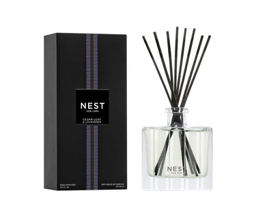 Nest New York’s Cedar Leaf & Lavender Collection Diffuser featuring Nest’s signature etched glass diffuser bottle with black reeds. Packaging is black with purple stripe.