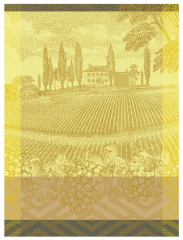 Le Jacquard Francais tea towel Vignoble in yellow depicting an estate flanked by cypress trees in front of which is a field, grapes, and patterned border.