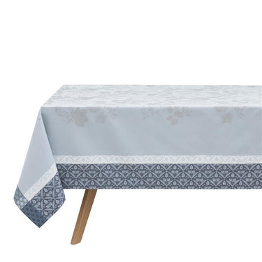 Manor Lane Blue Collection Tablecloth on table. Main area of tablecloth is light blue with a floral damask pattern. The border features a floral/geometric design in a lighter and darker blue.