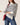A woman wearing a cream and navy blue horizontally striped knit turtleneck sweater, paired with blue jeans and holding a red shoulder bag, against a plain off-white background.