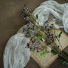 Dried flowers on an open book with a white fabric draped over it, on a brown background