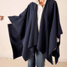Person wearing a navy blue poncho over a white shirt and jeans on a plain background