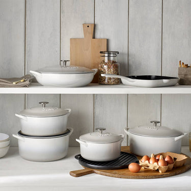 Set of white cookware on a kitchen shelf with wooden cutting board and eggs.