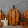 Decorative pumpkins with a candle on a wooden surface against a gray wall.