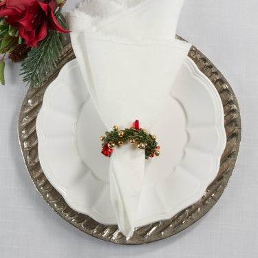 Decorative Christmas wreath on a folded white napkin with a silver charger plate and floral arrangement.