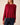 A woman wearing a long-sleeve knit sweater in deep burgundy red, paired with dark blue jeans, shown from the side against a plain beige background.