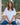 Woman with long brown hair seated wearing Mersea white pocket tee and blue jeans. Behind her are some trees.