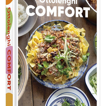 Cover features a noodle dish in a blue and white bowl surrounded by smaller bowls containing the ingredients for the dish. They are sitting on a wooden table