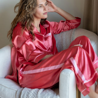 Model is wearing the Satin Sailor pajama set in Sunset (coral). The pajamas are trimmed in a contrasting light pink color.