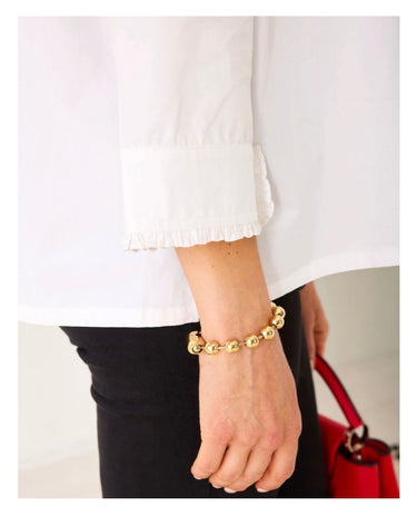 Gold bracelet on a wrist with a white shirt and red handbag in the background