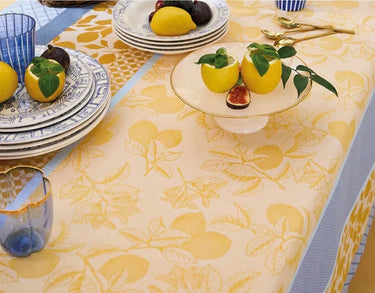 Dining table setting with lemons, figs, and decorative plates on a patterned tablecloth.