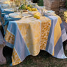 Outdoor table setting with a patterned tablecloth, lemons, and greenery.