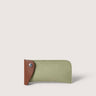 A slim, minimalist card holder or wallet made of sage green felt with a contrasting brown leather tab on the left side, secured by a silver snap button, set against a solid light beige background.