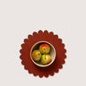 A top-down view of a scalloped dark red felt placemat with a small beige bowl containing three pears, set against a solid light gray background.