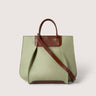 A structured tote bag in light sage green canvas with brown leather handles, trim, and a diagonal shoulder strap, shown on a plain light beige background.