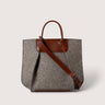 A structured gray felt tote bag with brown leather handles, a brown leather top panel, and a brown shoulder strap, shown on a light beige background.