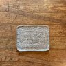 A rectangular ceramic plate with rounded corners, featuring a textured, crackled white glaze over a warm brown clay base, photographed from directly above on a rustic wooden tabletop.