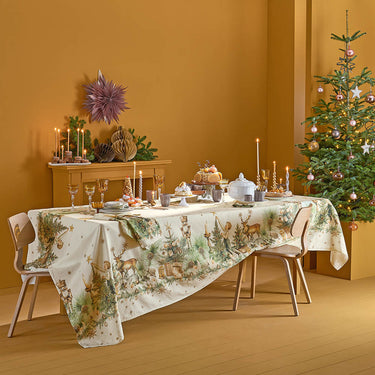 Garnier-Thiebaut Noel Vintage Dore tablecloth on a rectangular table set with candles and festive dinnerware. There is a decorated mantle and Christmas tree in the background.