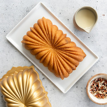 Cake baked in Nordic Ware Classic Fluted Loaf Pan shown with a pitcher of glaze and chopped pecans
