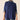 A woman wearing a navy blue cable-knit mock-neck sweater with striped knit cuffs, layered over a matching striped mock-neck shirt, paired with blue jeans against a plain beige background.