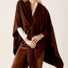 Woman wearing a brown poncho over a white shirt and brown pants on a beige background