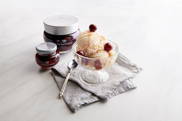 Ice cream sundae with cherry toppings and jars of jam on a white surface