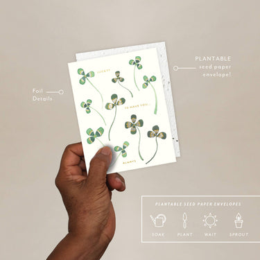 Hand holding a plantable seed paper envelope with clover design on a beige background