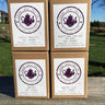 Four boxes of Loose Leaf Tea Co. tea chests on a wooden surface with a grassy area and trees in the background.