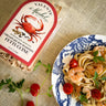 Valente Market fettuccine seasoning package with a bowl of pasta and shrimp on a textured surface