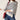 A woman wearing a cream and navy blue horizontally striped knit turtleneck sweater, paired with blue jeans and holding a red shoulder bag, against a plain off-white background.
